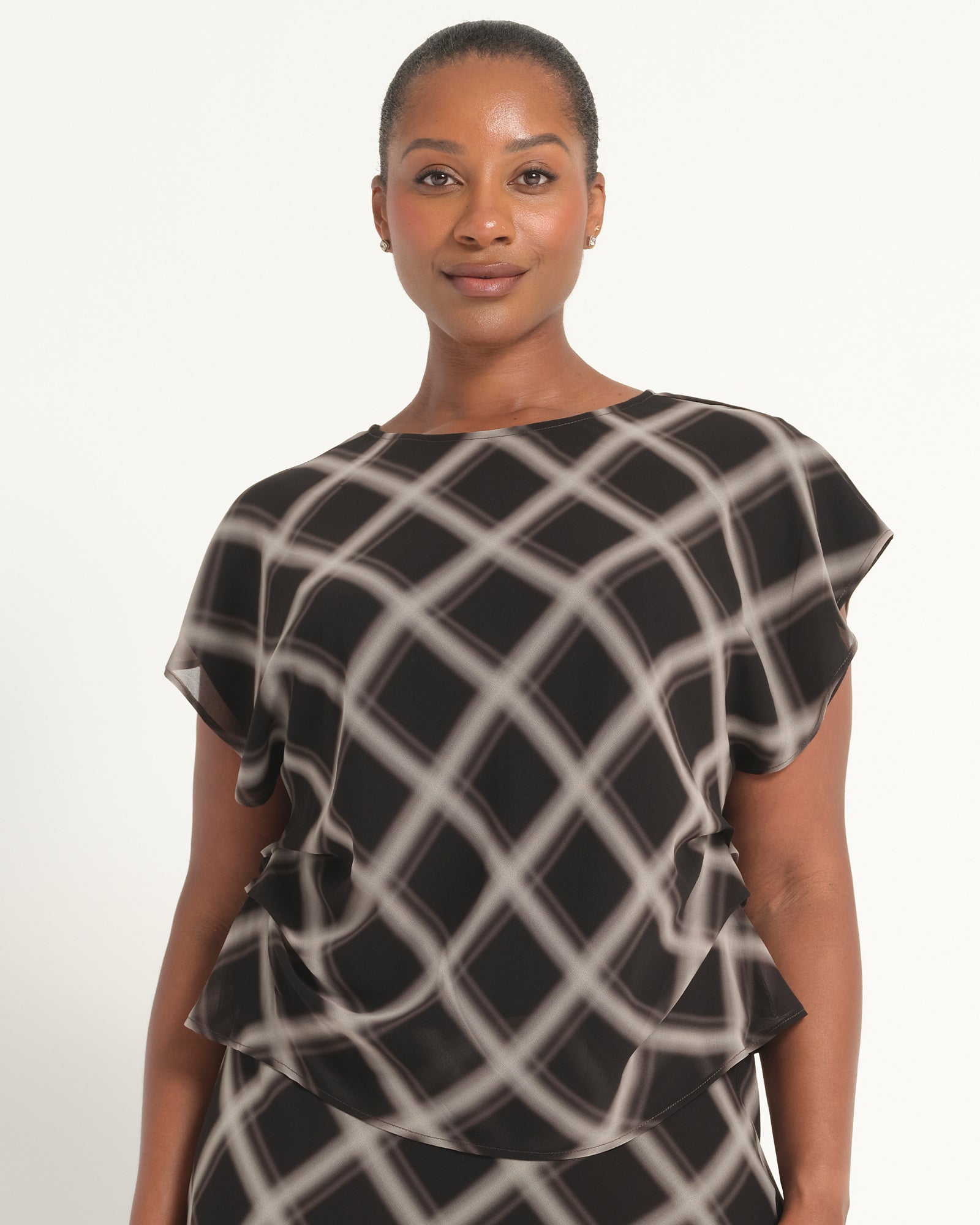 A woman wearing a black and white patterned blouse with short flutter sleeves and a layered ruffle hem, photographed against a plain light background.