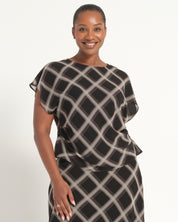 A woman modeling a black and beige geometric patterned dress with draped cap sleeves against a plain white studio background.