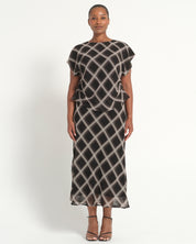 A woman modeling a sheer black midi dress with a beige geometric lattice pattern, featuring short flutter sleeves and a ruffled waist detail, set against a plain light background.