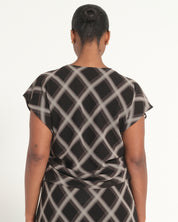 A woman viewed from the back wearing a short-sleeve black dress with a white diagonal lattice pattern, set against a plain white studio background.