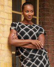 Woman in a black and white patterned dress standing against a brick wall.