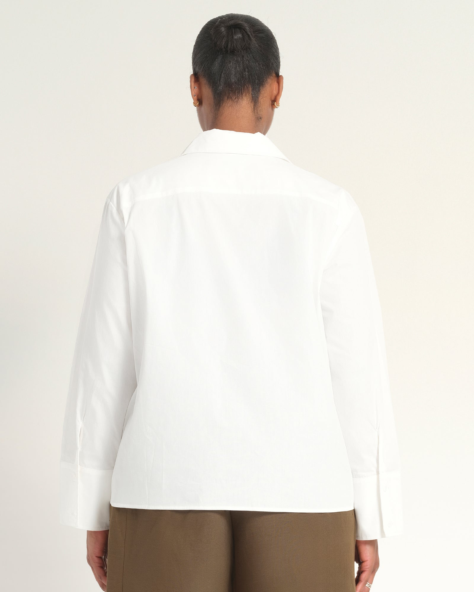 A person shown from the back wearing a white long-sleeve button-up shirt and brown pants against a plain light background.