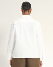 A person shown from the back wearing a white long-sleeve button-up shirt and brown pants against a plain light background.