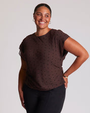 Woman wearing a brown polka dot top against a plain background
