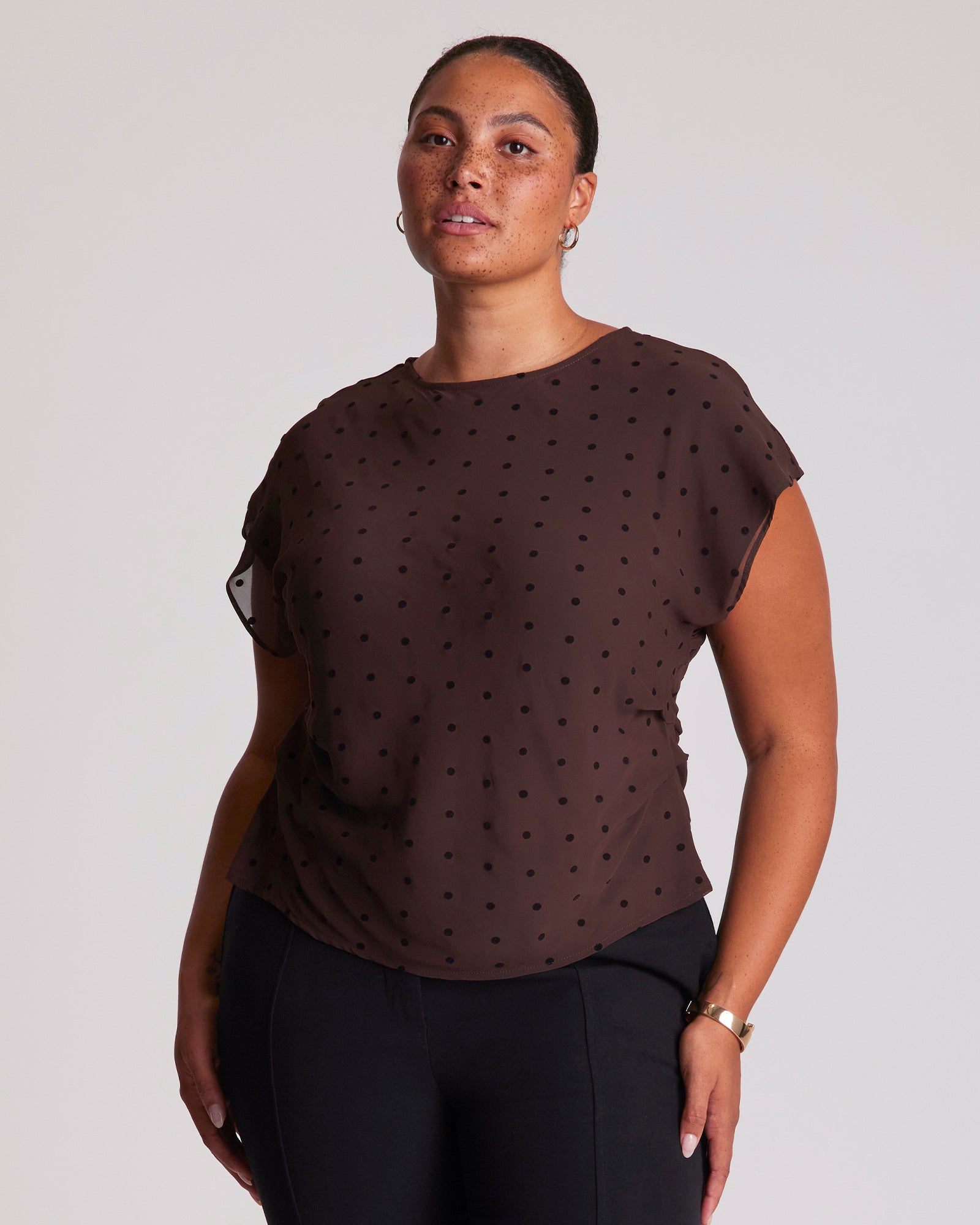 Woman wearing a brown polka dot top against a plain background