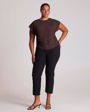 Woman wearing a brown polka dot top and black pants on a plain background