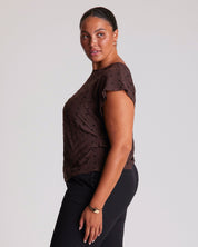 Woman wearing a brown top with black polka dots and black pants on a light gray background