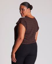Woman wearing a brown polka dot top and black pants on a light gray background