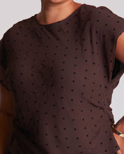 Brown polka dot top worn by a person on a plain background