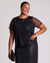 Woman wearing a black sequin dress against a plain background