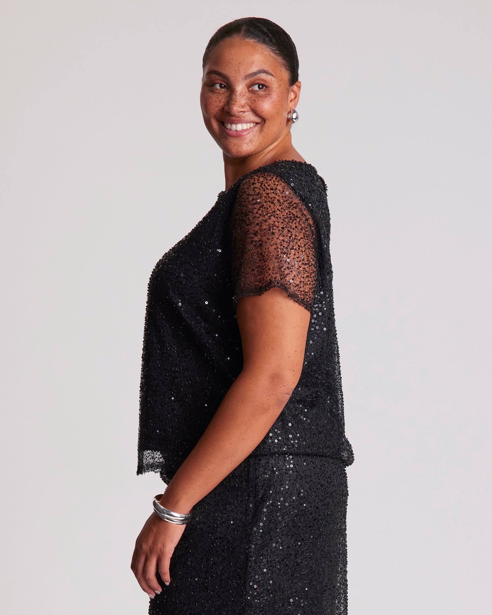 Woman wearing a black sequin dress against a plain background