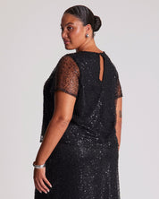 Woman wearing a black sequin dress with sheer sleeves on a plain background
