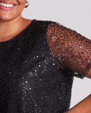 Black sequin dress with sheer sleeves on a plain background
