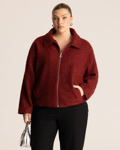 Woman wearing a deep red collared jacket with a silver chrome handbag against a neutral background