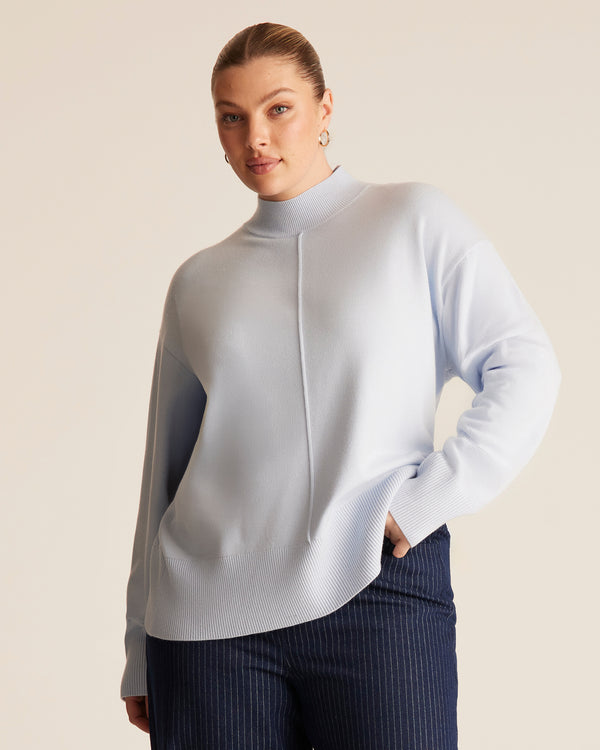Woman wearing a light blue high neck knit sweater against a beige background.