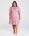 A plus size woman wearing the Estelle La Croisette Dress, a pink and white floral print dress.