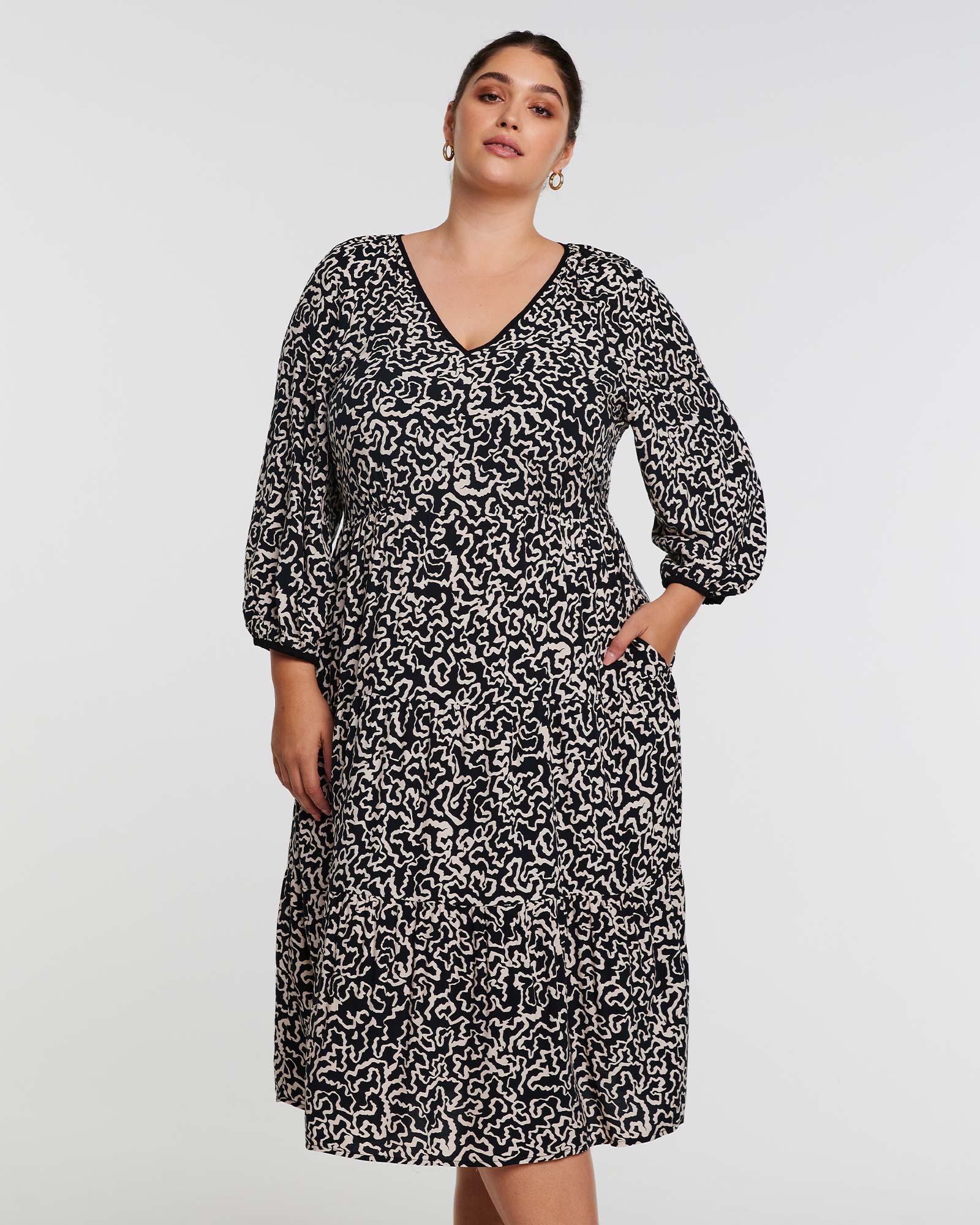 A plus size woman wearing an Estelle Sparrow Long Sleeve Black and Cream Midi Dress.