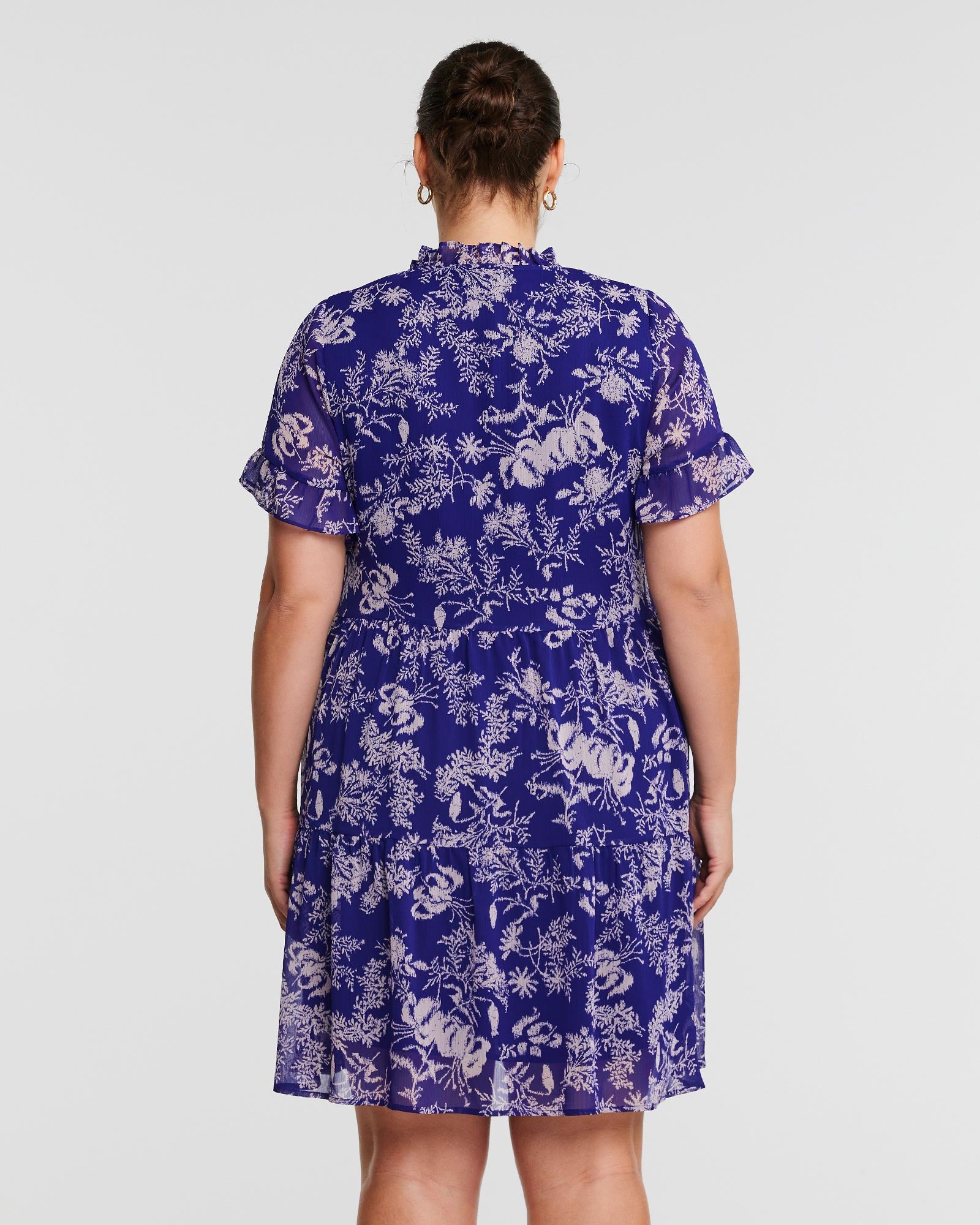 The back view of a woman wearing an Estelle Ultra Leaf Purple Tiered Knee Length Dress.
