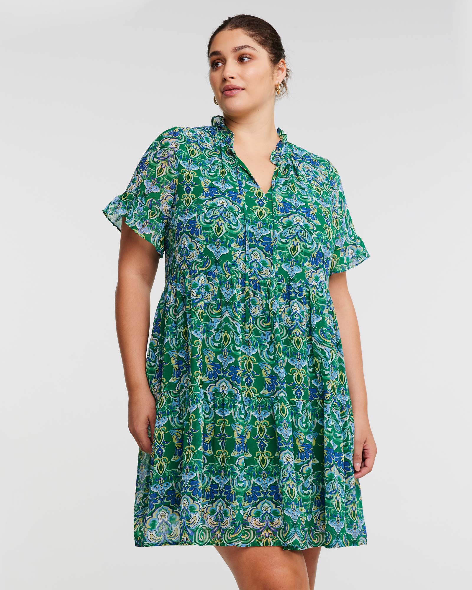 A plus size woman in a Mandala Green Tiered Mini Dress by Estelle.