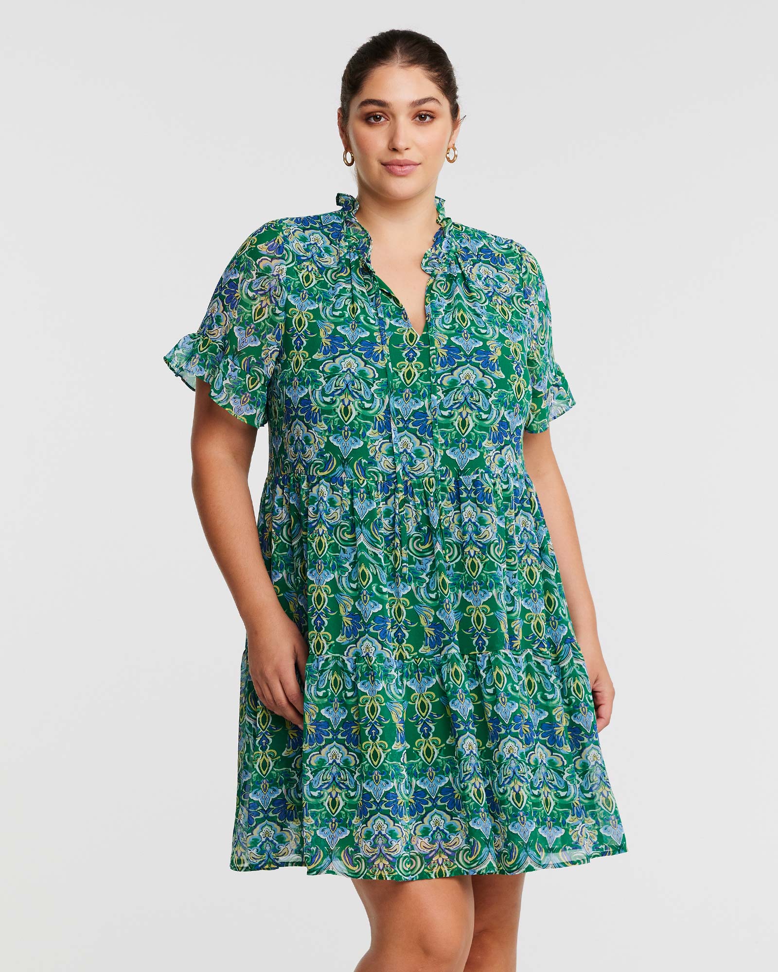 A plus size woman wearing an Estelle Mandala Green Tiered Mini Dress.