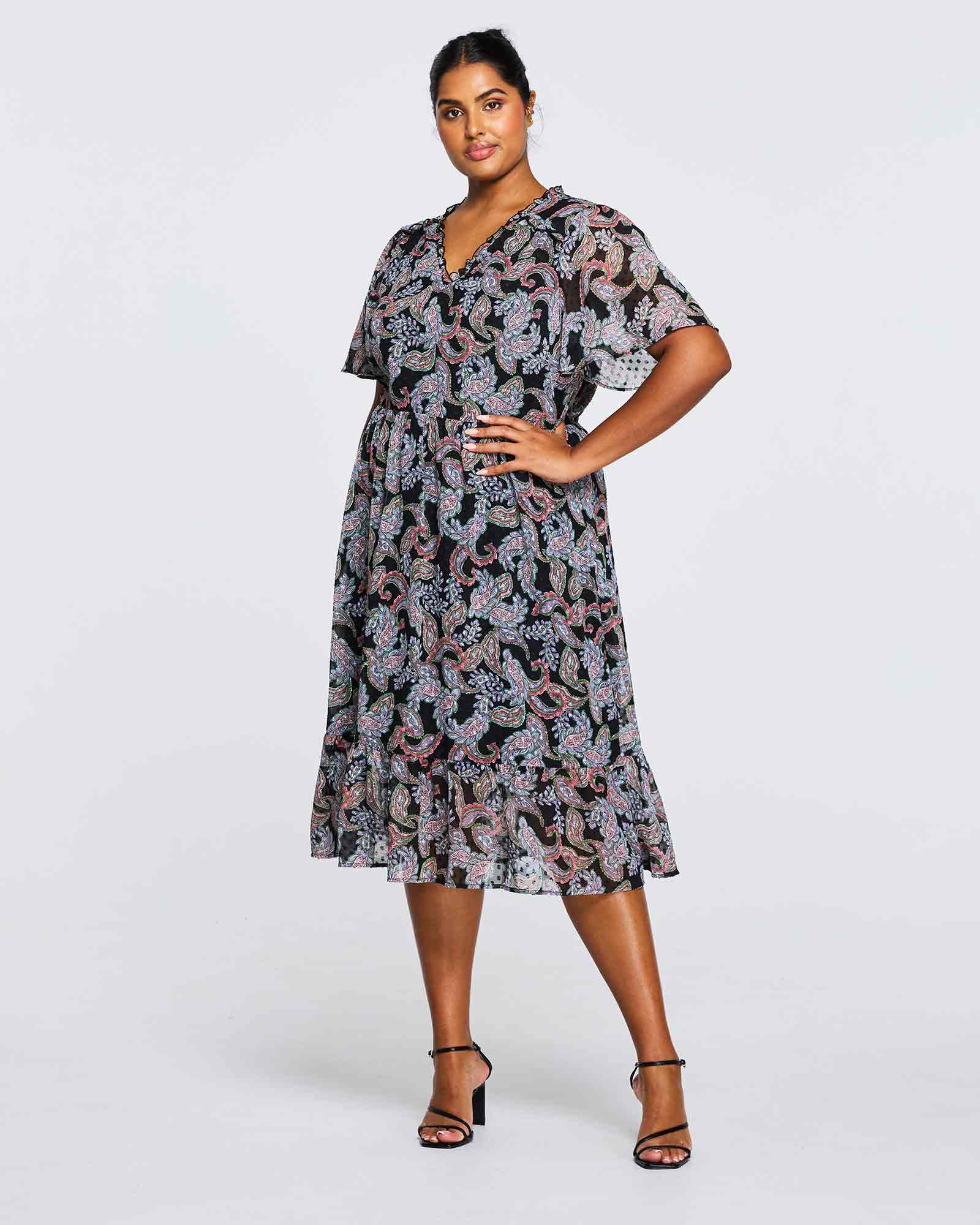 A plus size woman is posing in an Estelle Maya Purple Paisley Midi Dress.