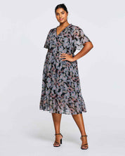 A plus size woman is posing in an Estelle Maya Purple Paisley Midi Dress.