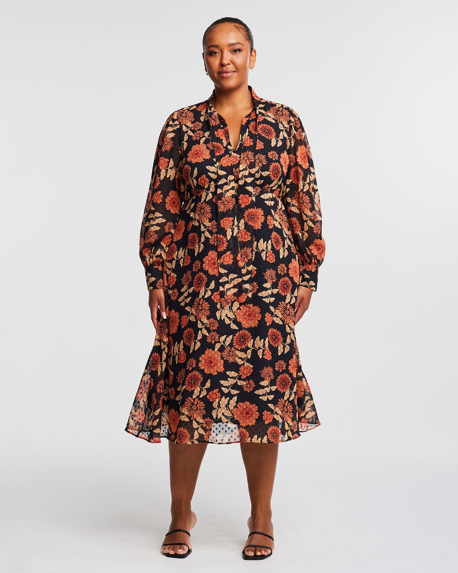 A plus size woman wearing an Autumnal Floral Midi Dress with Neck-Tie in autumnal hues.