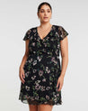 A plus size woman wearing a Estelle Climbing Rose Black Mini Dress.