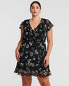 A plus size woman wearing an Estelle Climbing Rose Black Mini Dress.