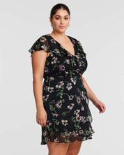 A plus size woman wearing an Estelle Climbing Rose Black Mini Dress.
