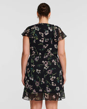 The back view of a woman in a Climbing Rose Black Mini Dress by Estelle.