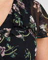 A close up of a woman wearing an Estelle Climbing Rose Black Mini Dress.