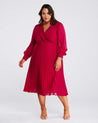 A plus size woman wearing an Estelle Raspberry Pleated Midi Dress.
