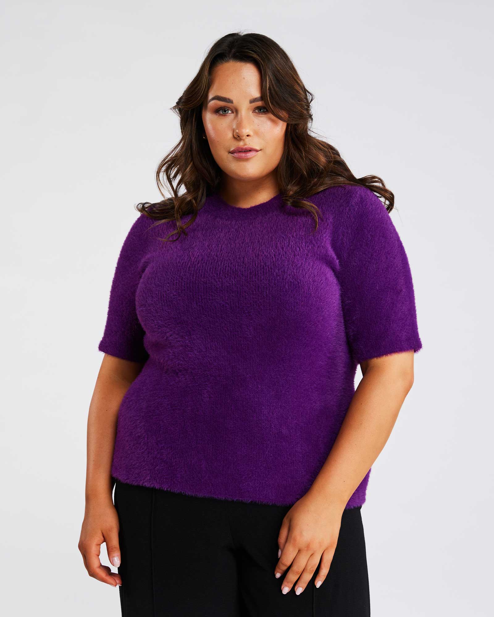 A woman wearing an Estelle Nora Fuzzy Purple Short-Sleeved Sweater and black pants.