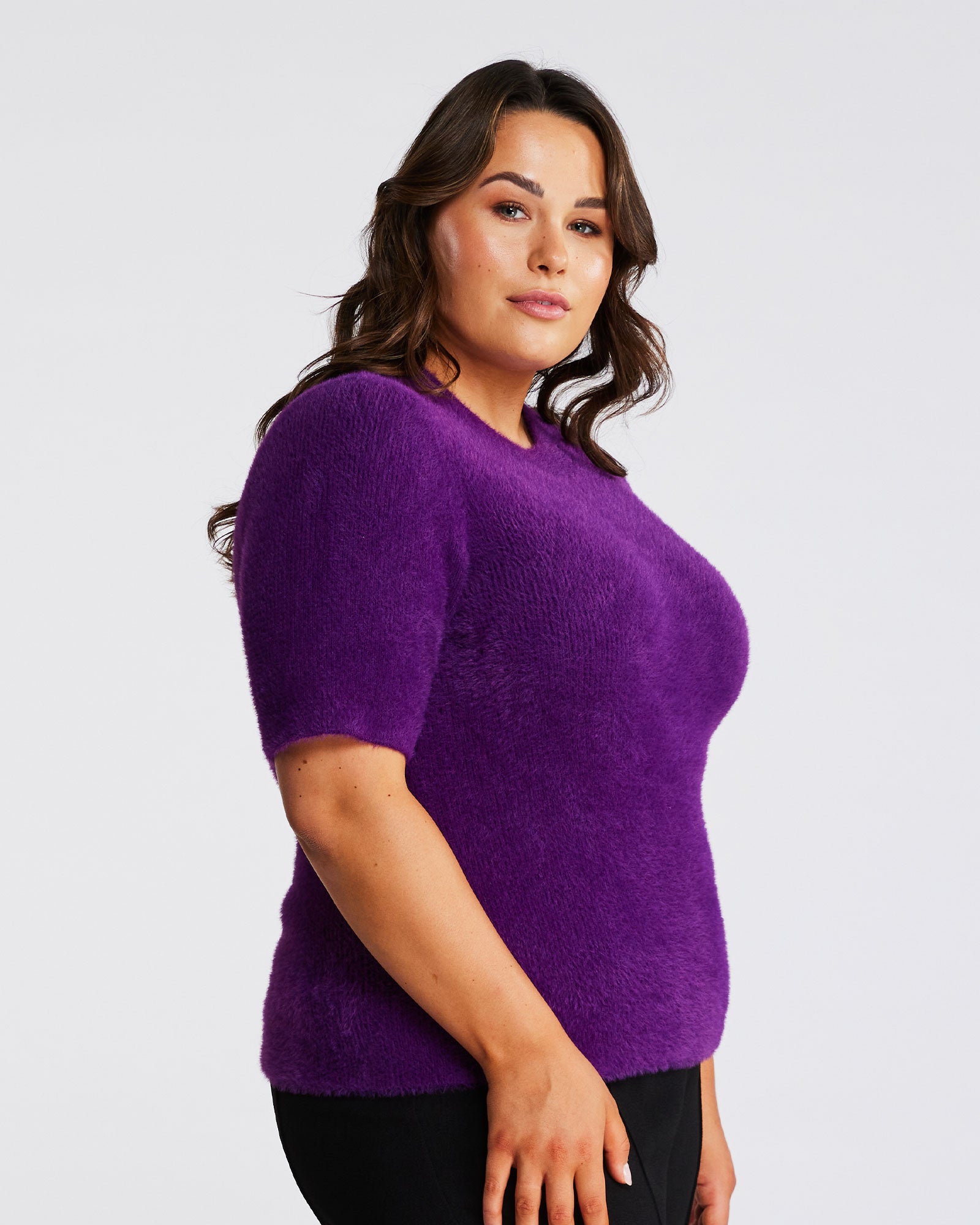 A woman wearing the Estelle Nora Fuzzy Purple Short-Sleeved Sweater and black pants.