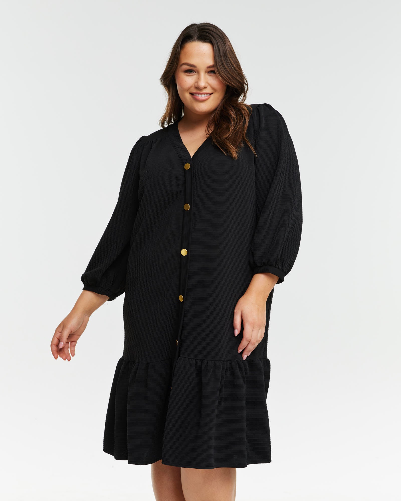 A plus size woman wearing the Elissa Dress, a versatile black ruffle sleeved dress with textured knit fabric.