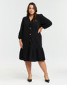 A versatile plus size woman wearing the Elissa Dress, a textured black ruffle shirt dress with gold hardware detailing.