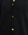 A woman wearing a black blouse with gold buttons and Elissa Dress, a versatile black mini dress.