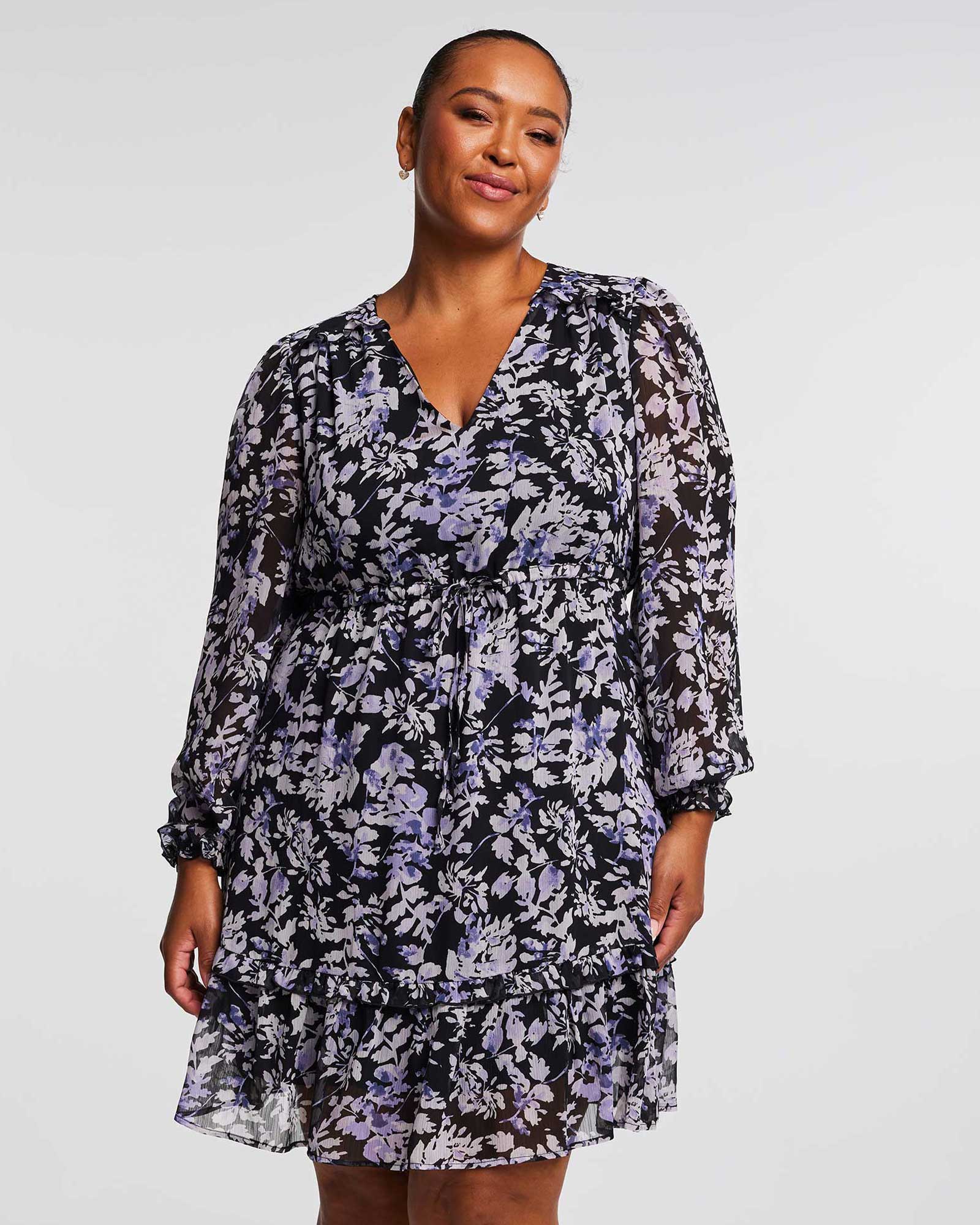 A plus size woman wearing Estelle's Wild Orchid Long Sleeved Floral Dress.