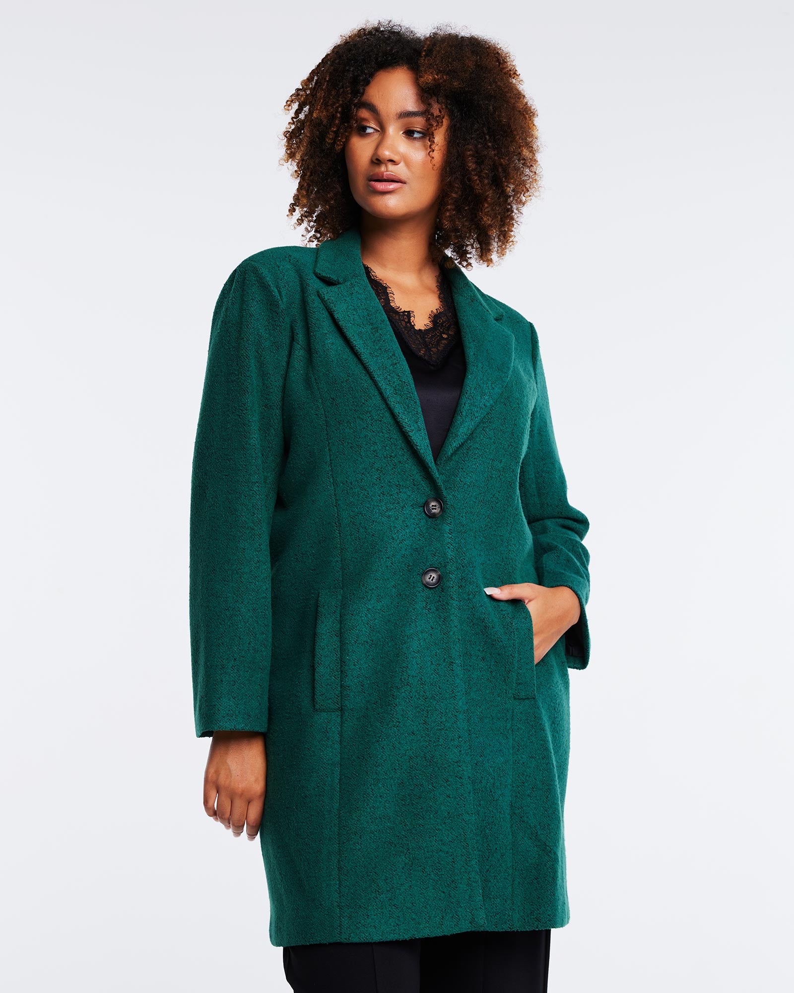 A woman wearing a Wander Green Collared Coat by Estelle and black pants.