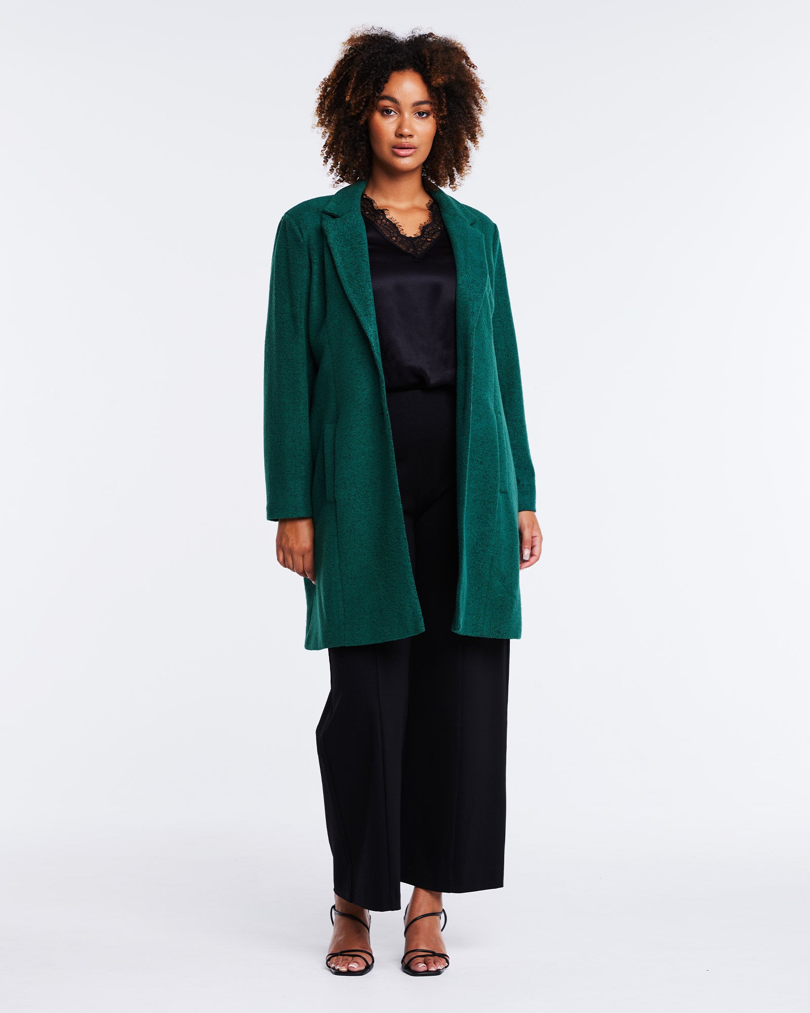 The model is wearing the Wander Green Collared Coat and black wide leg pants from Estelle.