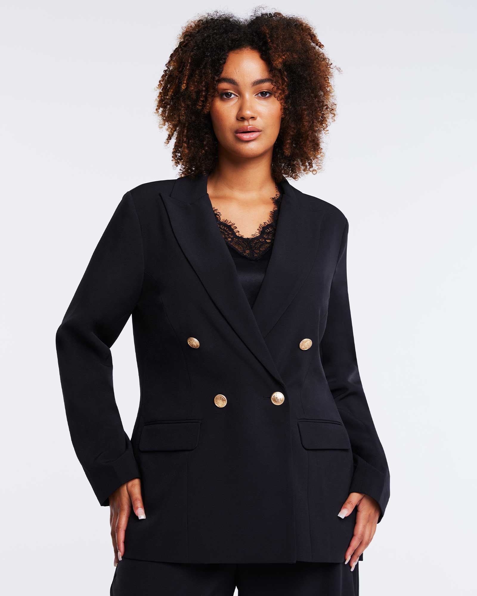 A plus-size woman wearing a Savannah Double-Breasted Black Blazer with gold buttons.