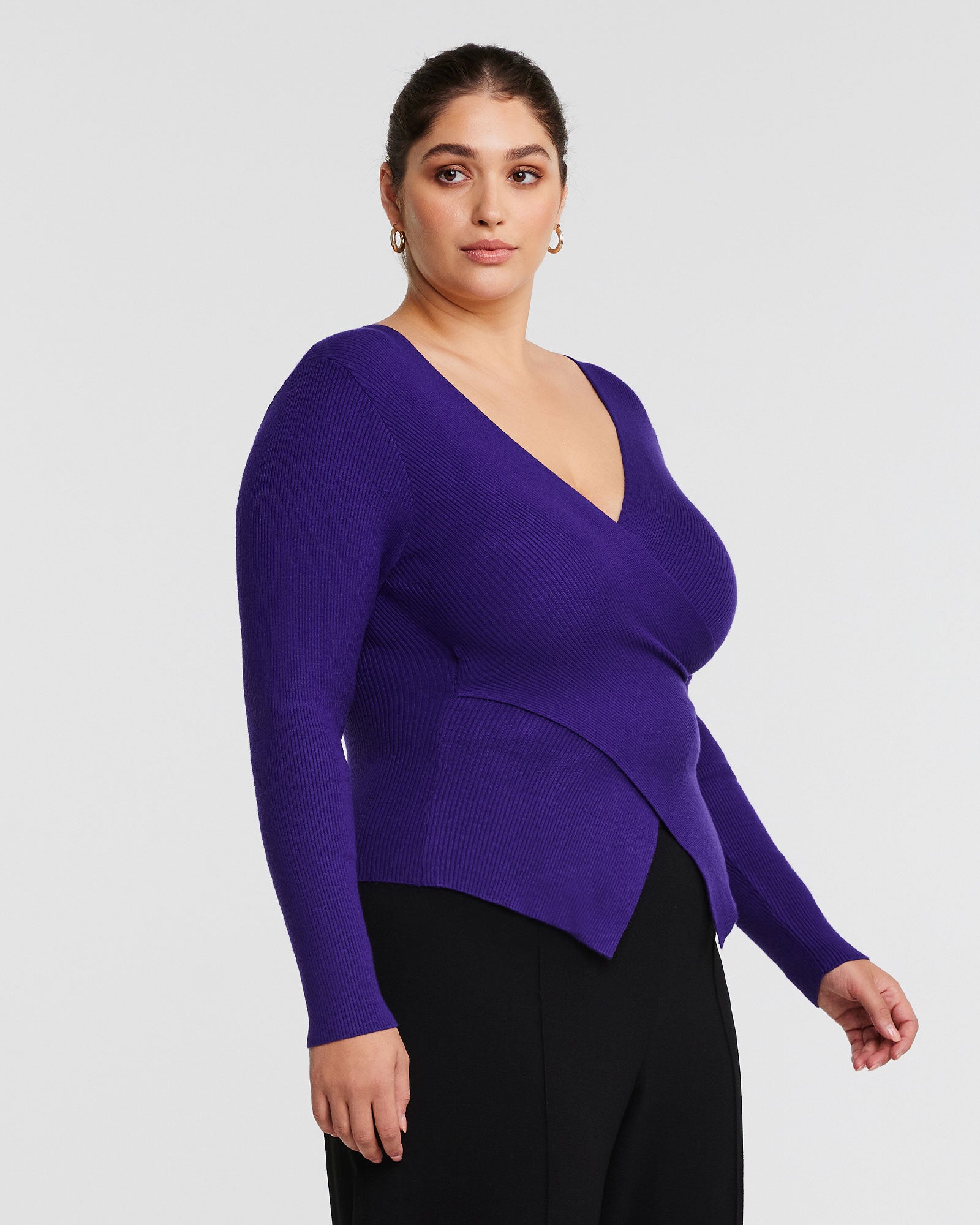 A woman wearing an Estelle Purple Wrap It Up Long Sleeve Knit Sweater and black pants.
