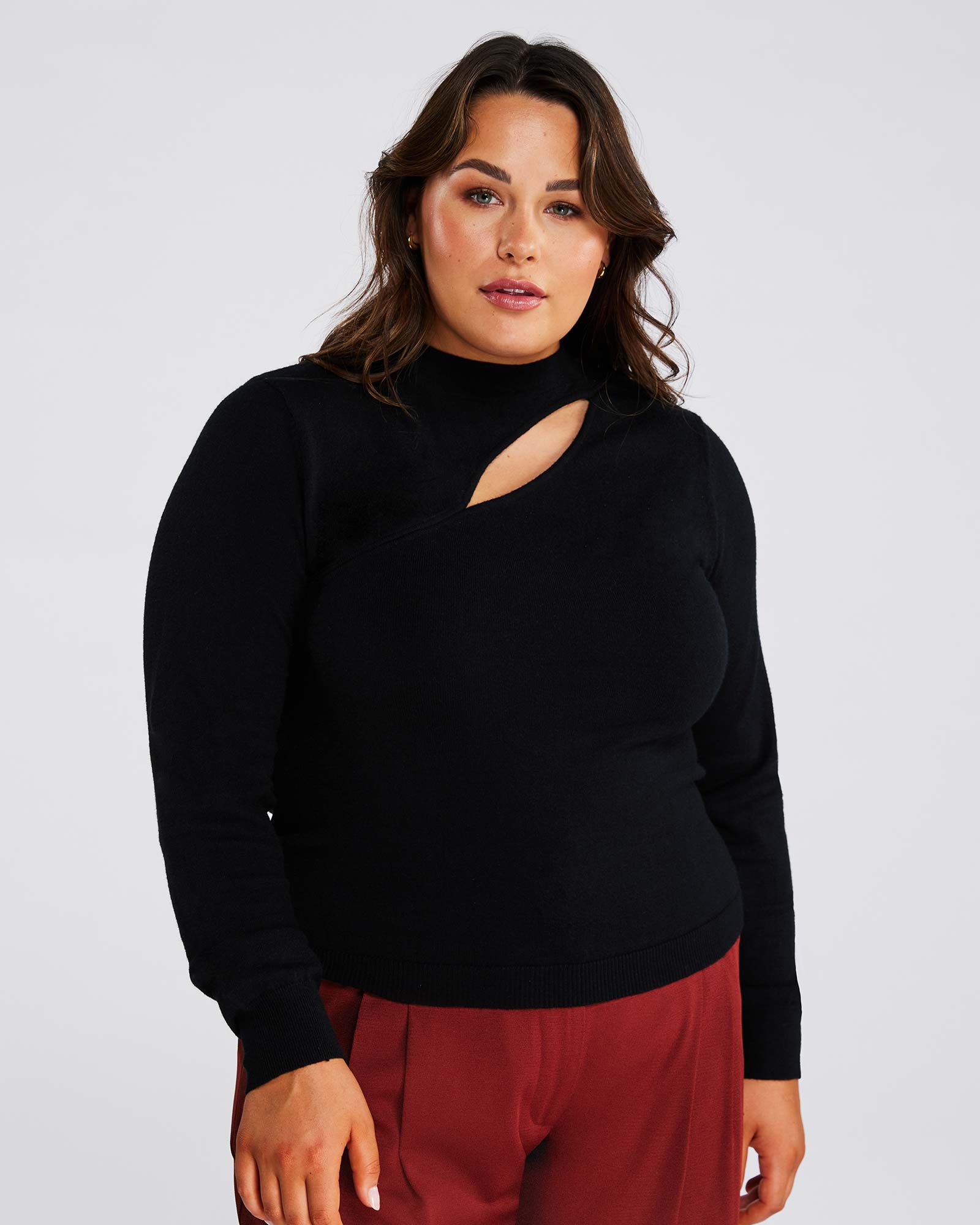 A plus-size woman with a high fashion quotient sporting a Black Cut Out Crewneck Sweater and red pants.
