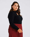 A plus-size woman flaunting her fashion quotient in a Black Cut Out Crewneck Sweater and burgundy trousers.