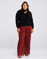 A plus-size woman showcasing her fashion quotient in a Black Cut Out Crewneck Sweater and burgundy wide leg pants.