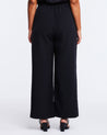 The back view of a plus-sized woman wearing a Savannah Black Wide-Leg Pant jumpsuit.