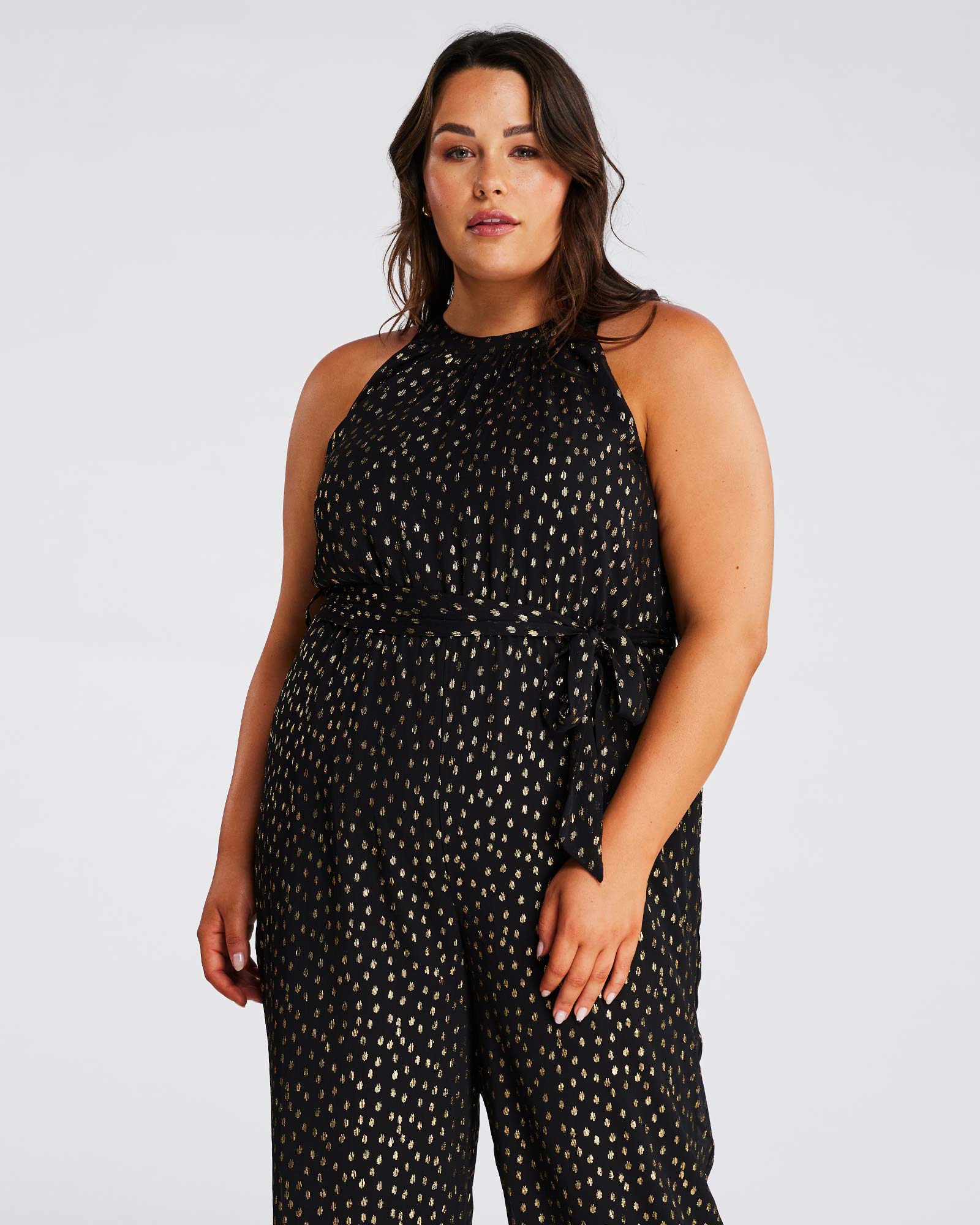 A plus size woman wearing an Estelle Gold Dust Halter Jumpsuit.