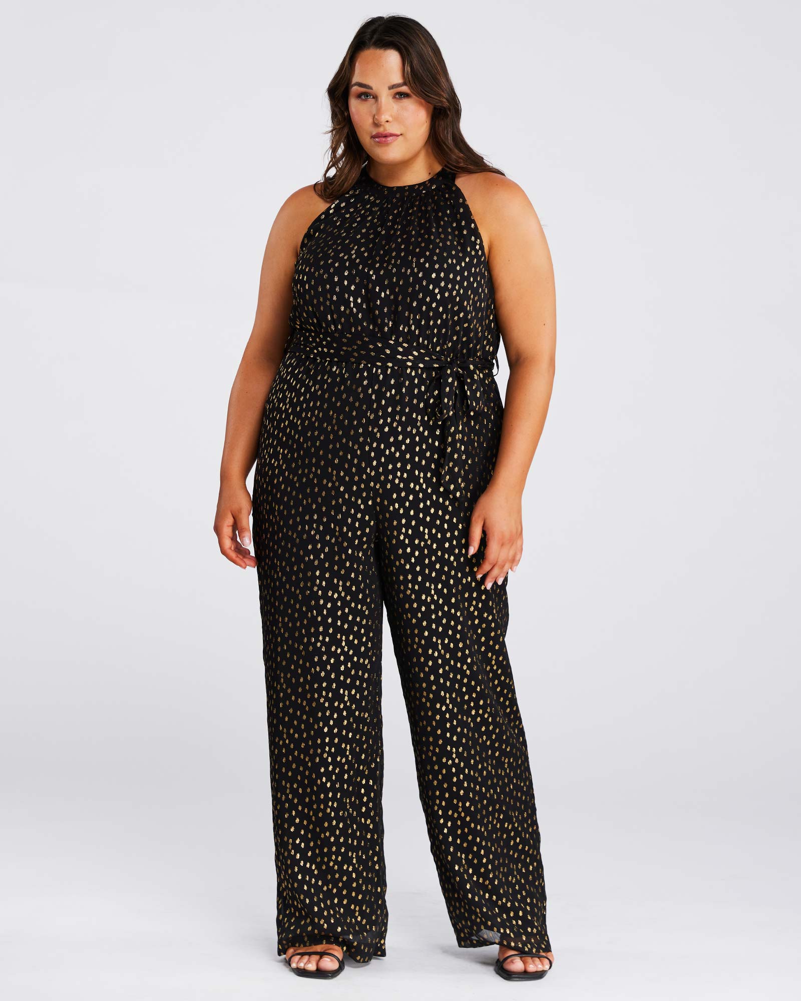 A plus size woman wearing an Estelle Gold Dust Halter Jumpsuit.