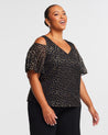 A plus size woman wearing an Estelle Gold Dust Cold Shoulder Top.